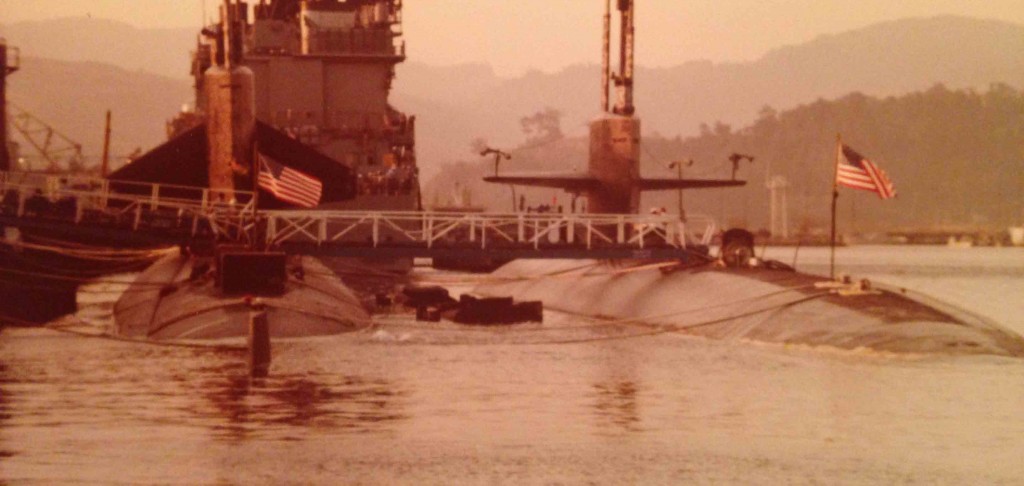 Behind a guided missile destroyer, A 637 Class Fast Attack (notice the vertically positioned sail planes) tied inboard of USS Bremerton in a WestPac port, probably Subic Bay, Philippines, circa 1983.