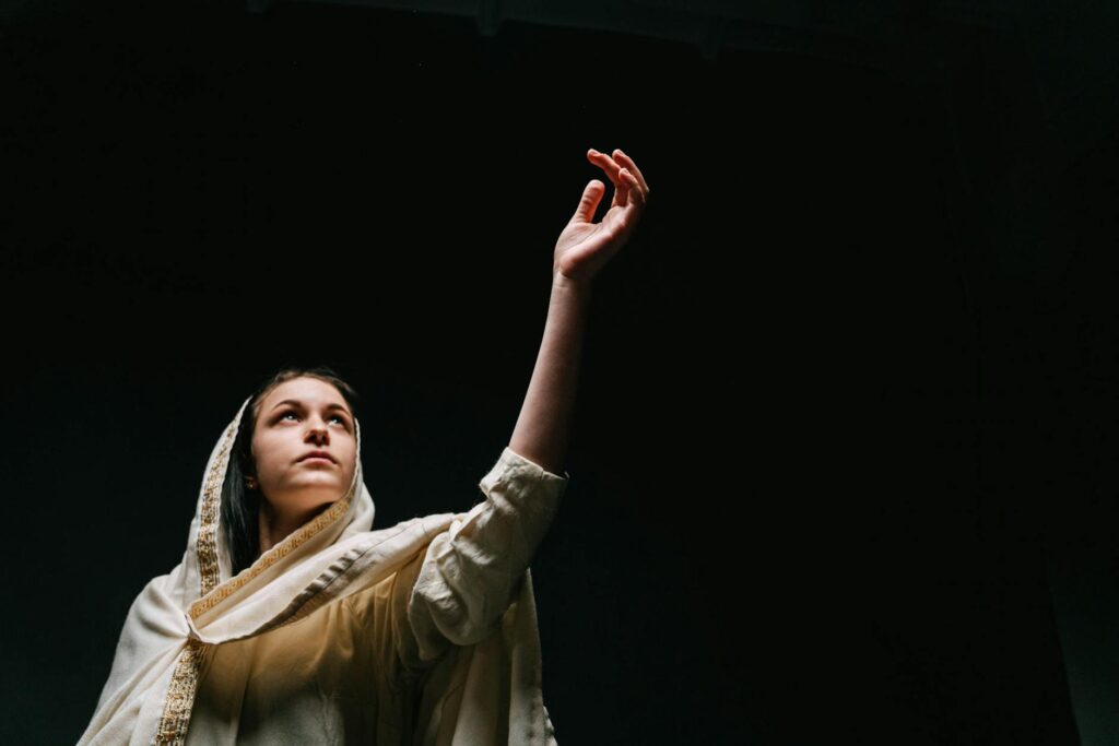 woman in white and gold scarf standing in black background