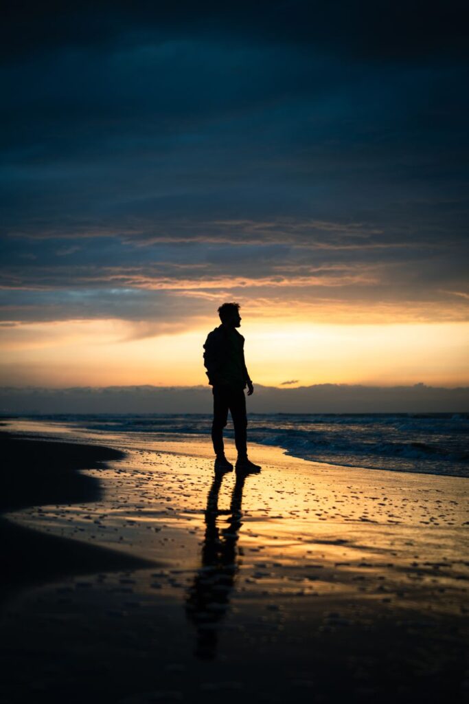 silhouette of man walking on beach at sunset