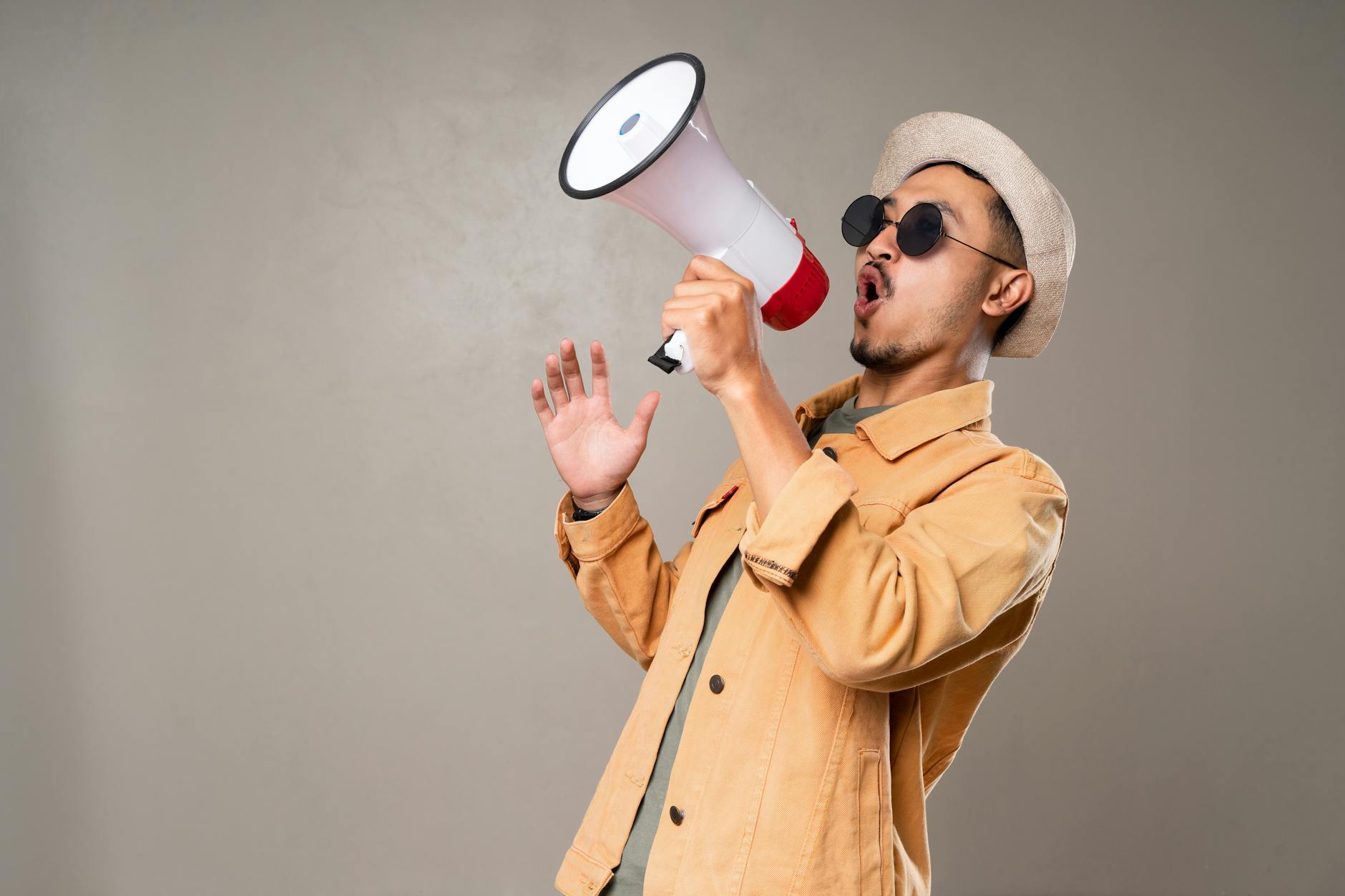 man wearing orange jacket while yelling on a megaphone