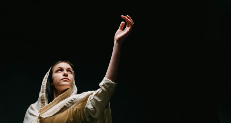 woman in white and gold scarf standing in black background