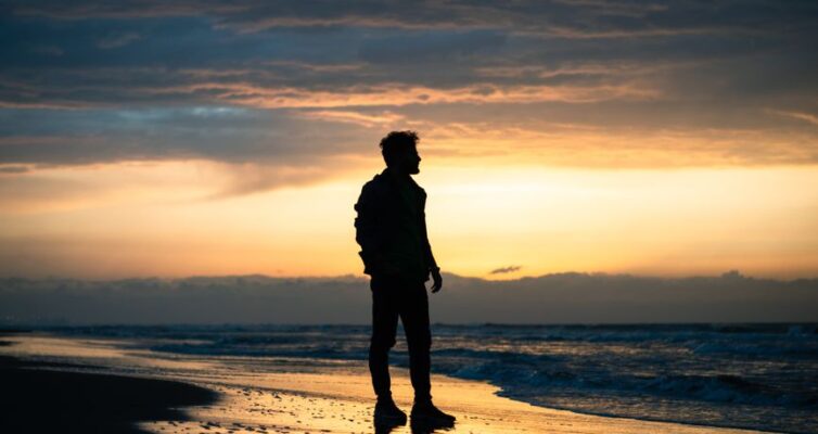 silhouette of man walking on beach at sunset